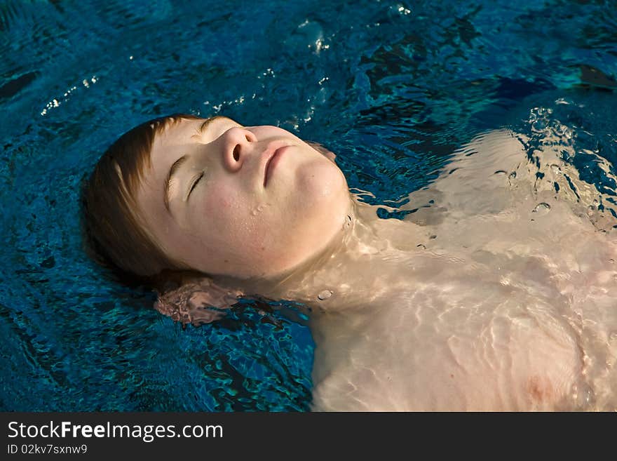 Boy with red hair and closed eyes is swimming and relaxing in a beautiful pool. Boy with red hair and closed eyes is swimming and relaxing in a beautiful pool