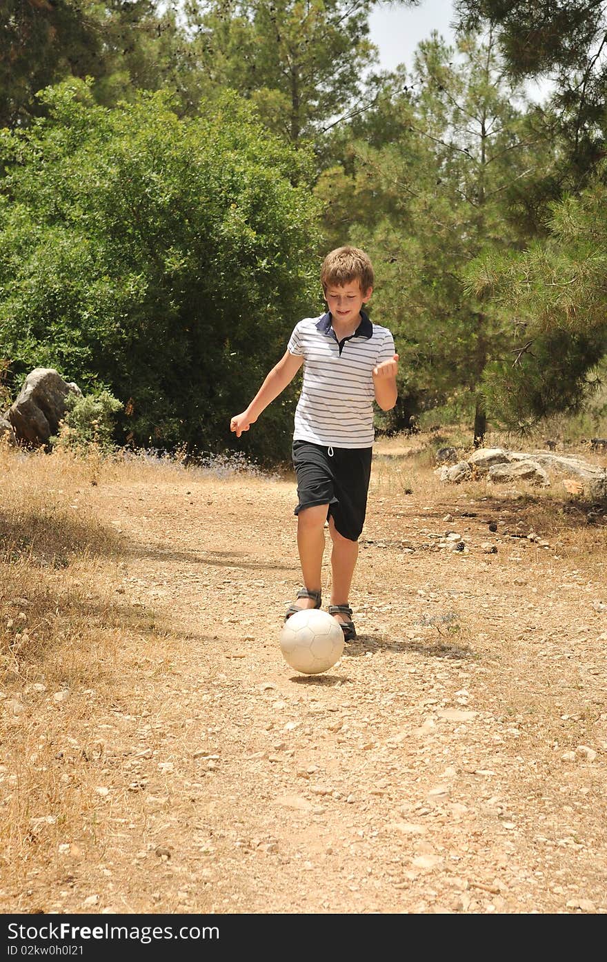 The boy ran in front of him and rolls the ball along the forest path. The boy ran in front of him and rolls the ball along the forest path