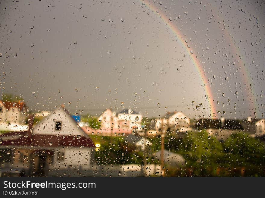 This is a picture of droplets on the glass on the background of the rainbow and houses. This is a picture of droplets on the glass on the background of the rainbow and houses