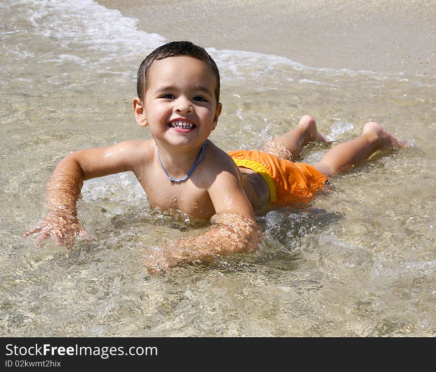 A smiling three year old Greek boy in orange swimsuit playing in the surf. A smiling three year old Greek boy in orange swimsuit playing in the surf.