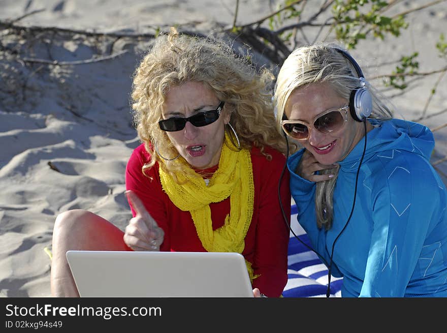 Two beautiful business women work on their laptop and enjoy some beach time. Two beautiful business women work on their laptop and enjoy some beach time.