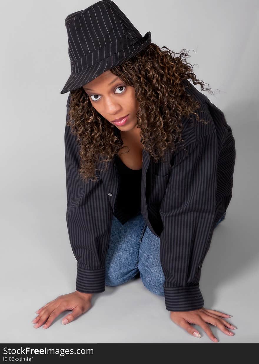 A portrait of a young African-American model in matching striped hat and shirt, kneeling on the floor and looking into the camera flirtatiously. A portrait of a young African-American model in matching striped hat and shirt, kneeling on the floor and looking into the camera flirtatiously