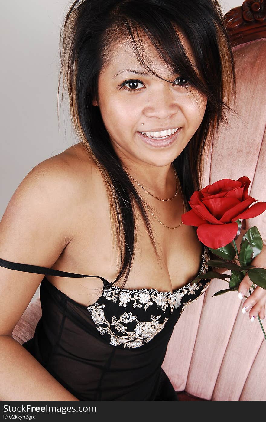 A young Asian woman in black lingerie with a red rose in her hand, sitting
in a pink old armchair, smiling into the camera, over light gray background. A young Asian woman in black lingerie with a red rose in her hand, sitting
in a pink old armchair, smiling into the camera, over light gray background.