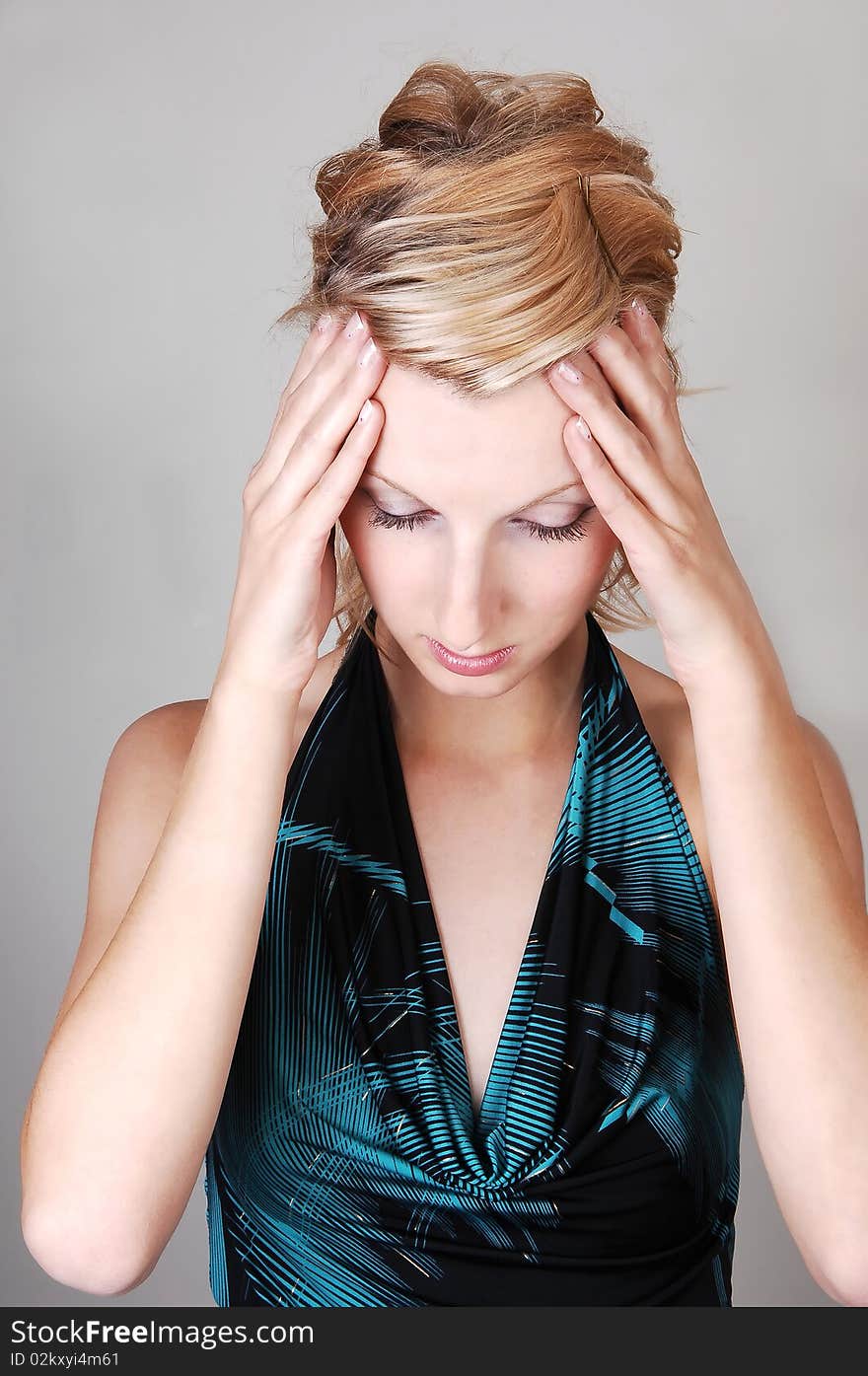 A beautiful blond woman holding her hands on her head to rap of her hurting head, on light gray background. A beautiful blond woman holding her hands on her head to rap of her hurting head, on light gray background.