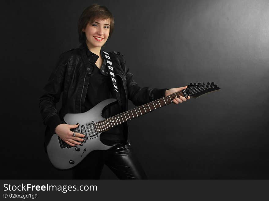 Rock girl in leather outfit with electric guitar on black background