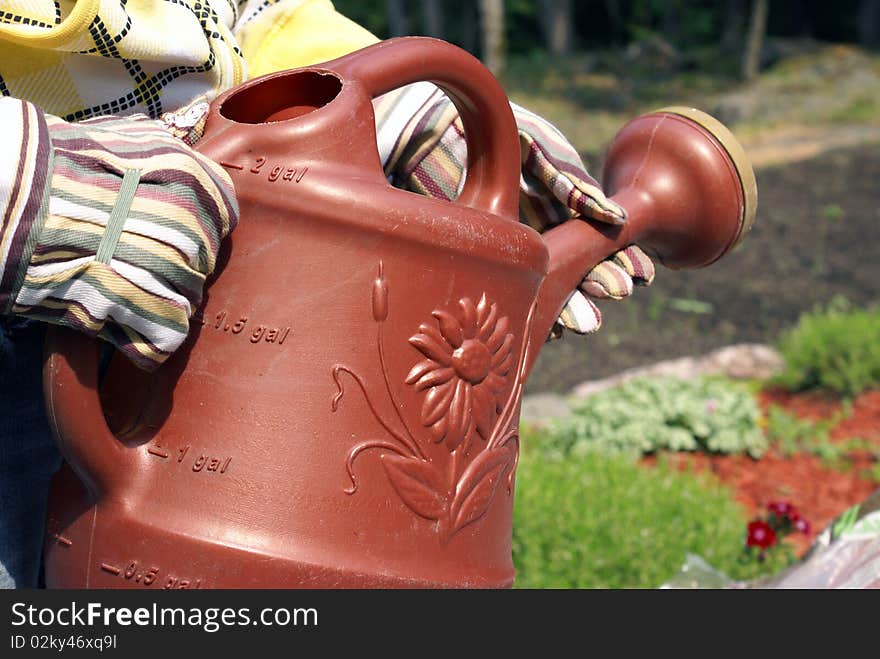 A gardener carries a water jug to the flowers for watering. A gardener carries a water jug to the flowers for watering.