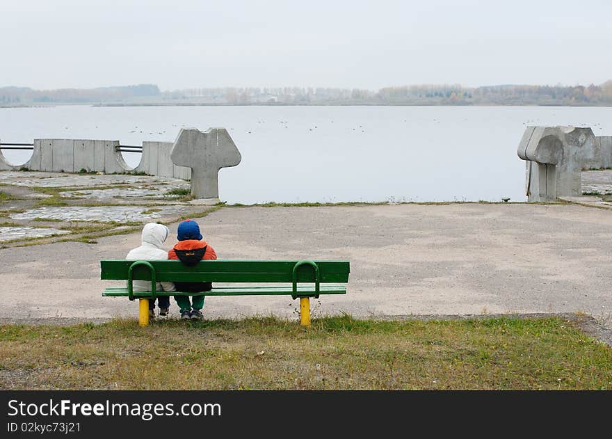 Overcast autumn day, children on a bench on the lake. Overcast autumn day, children on a bench on the lake