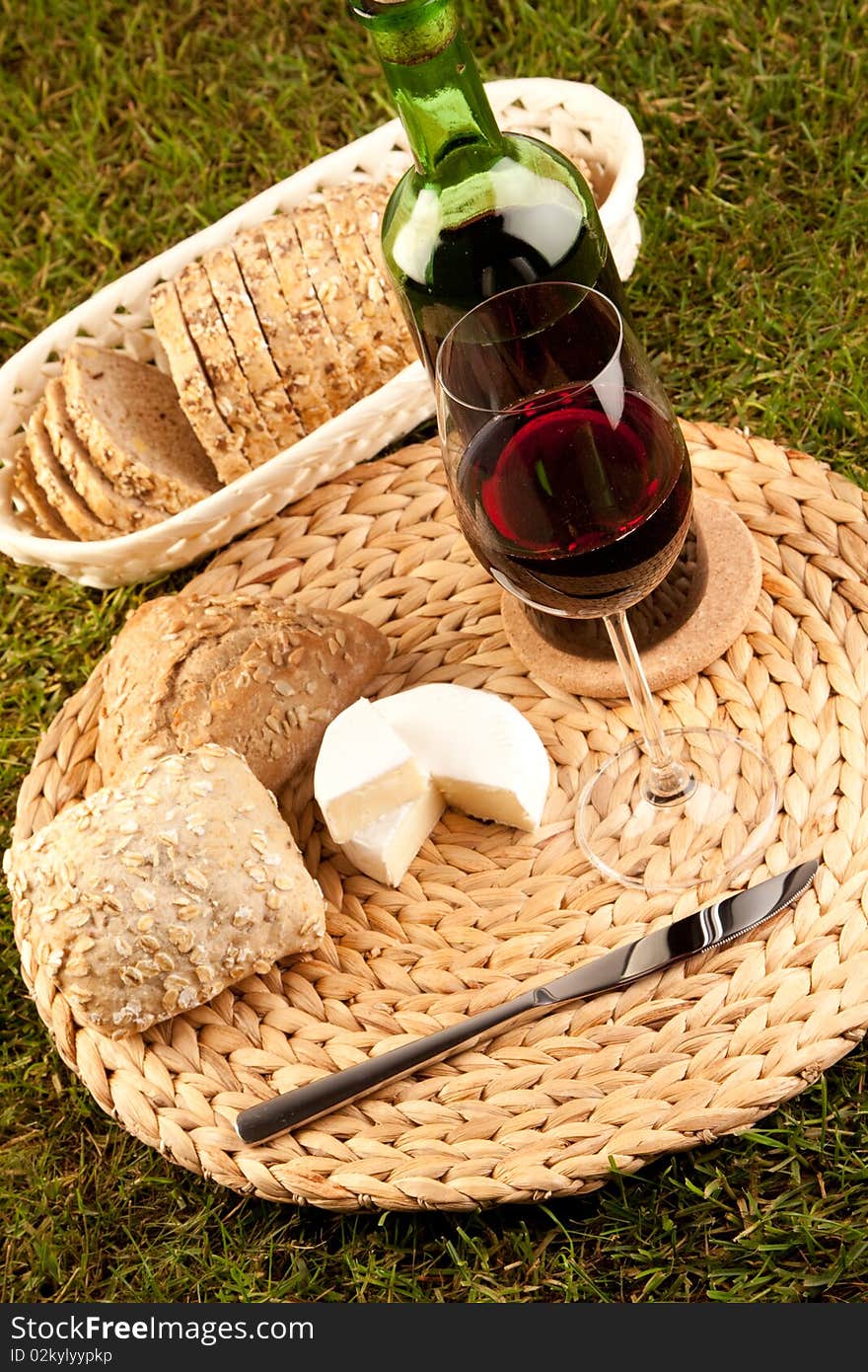 Wine picnic on grass with cheese, bread and other food.