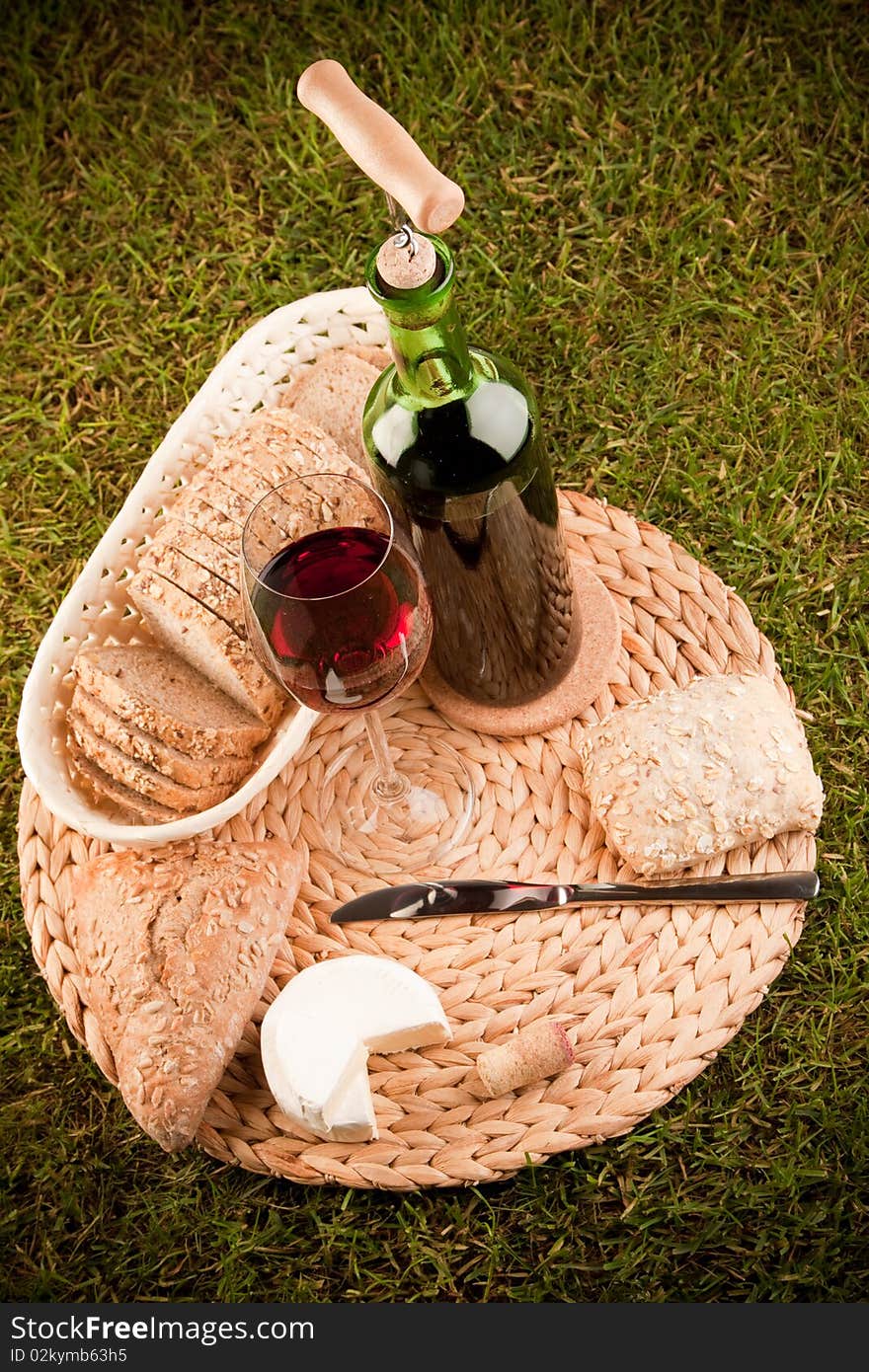 Wine picnic on grass with cheese, bread and other food.