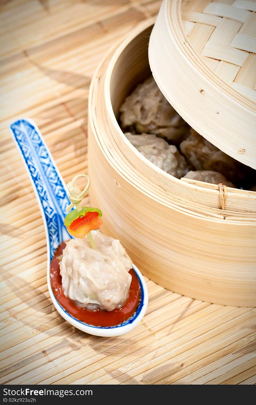 Traditional Chinese meal of dim sum or steamed dumplings on decorative spoon with harissa sauce and bamboo steamer.