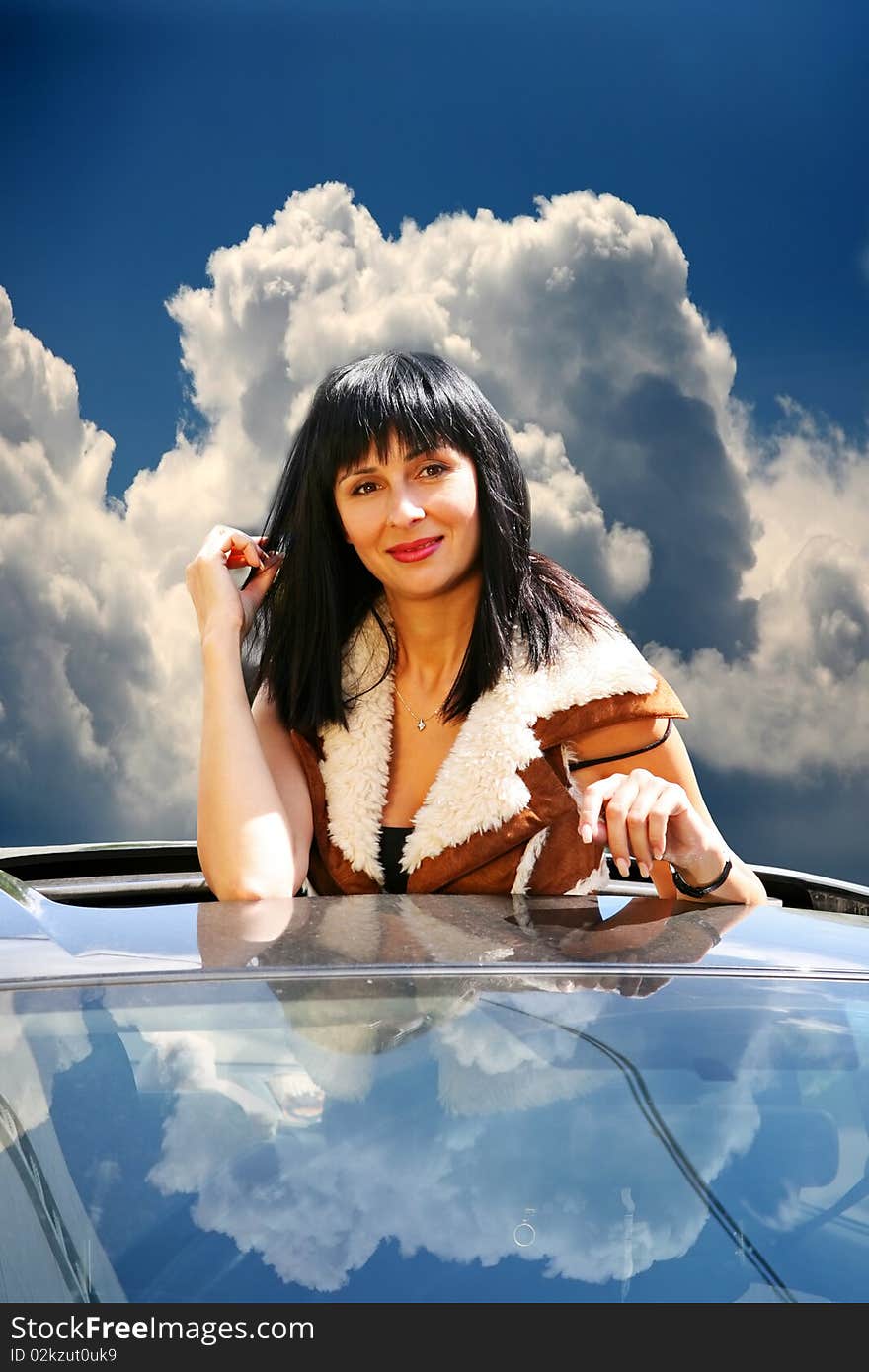 Beautiful brunette in the automobile on a background of the sky with clouds