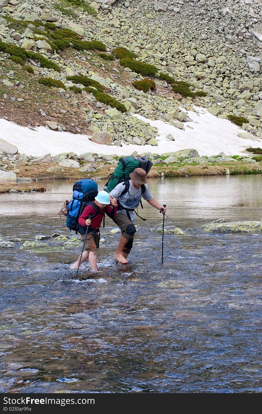 Two hikers are crossing mounain river