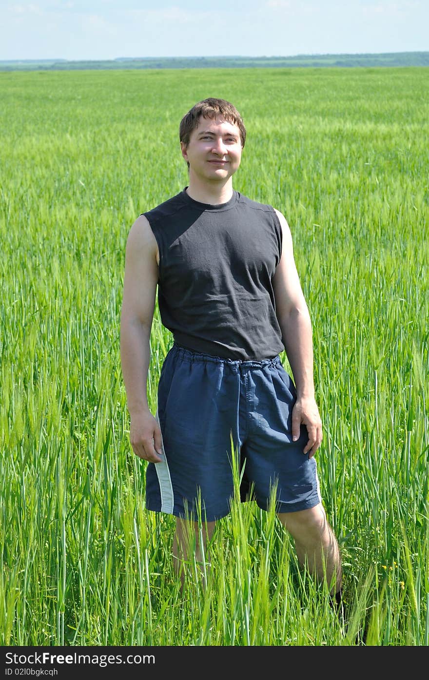 One man, standing in a field of green wheat, smiles. One man, standing in a field of green wheat, smiles