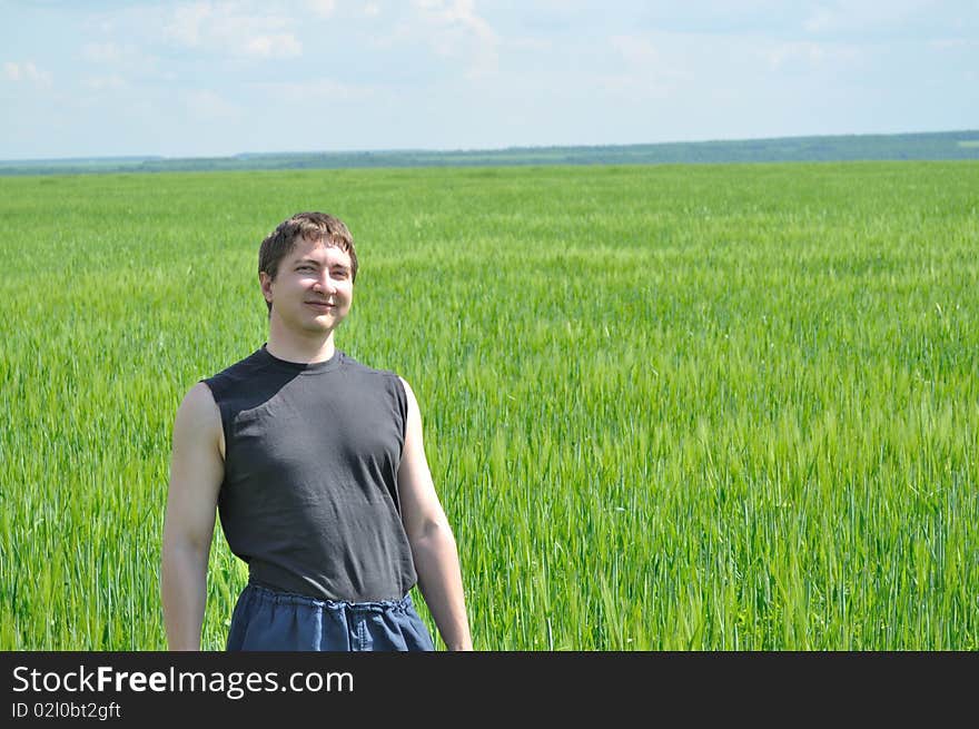 One man, standing in a field of green wheat, smiles. One man, standing in a field of green wheat, smiles