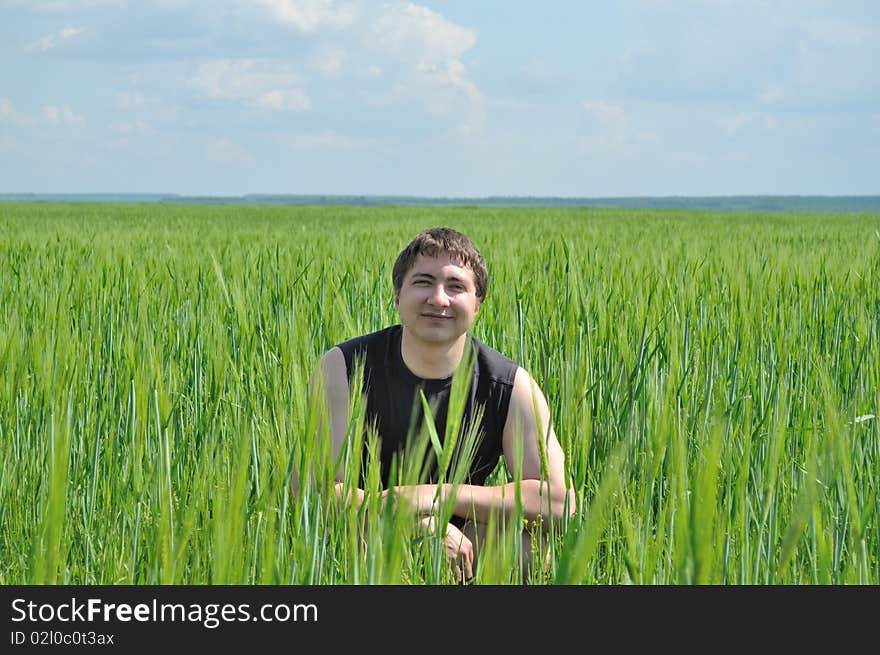 One man, sitting in a field of green wheat, smiles. One man, sitting in a field of green wheat, smiles