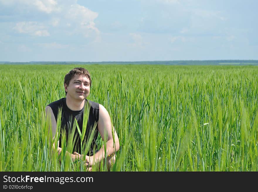 A Man Sits In A Field Of Green Wheat