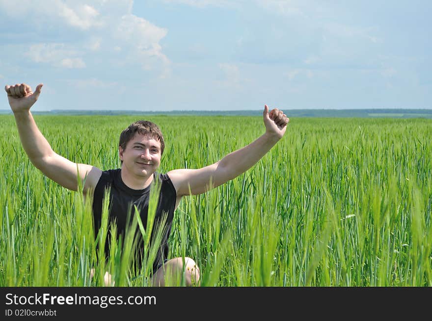 One man, sitting in a field of green wheat, smiles,raised his hands up. One man, sitting in a field of green wheat, smiles,raised his hands up