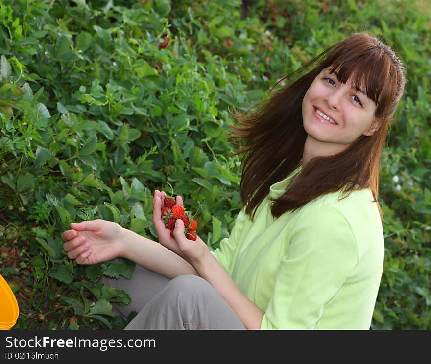 A smiling woman picking strawberries in a field closeup