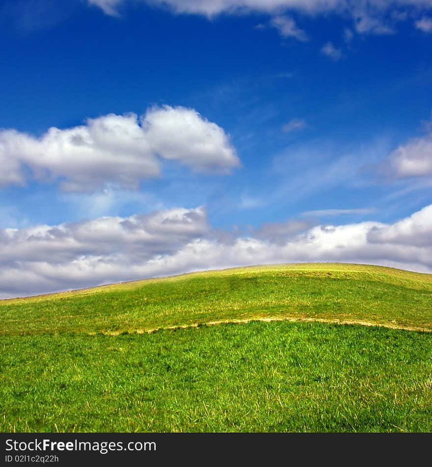 Green field against blue sky and clouds