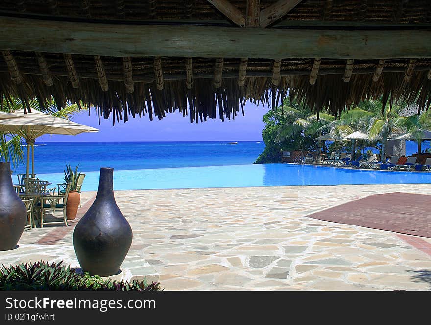 View of infinity pool and patio area overlooking tropical ocean on hot day. View of infinity pool and patio area overlooking tropical ocean on hot day