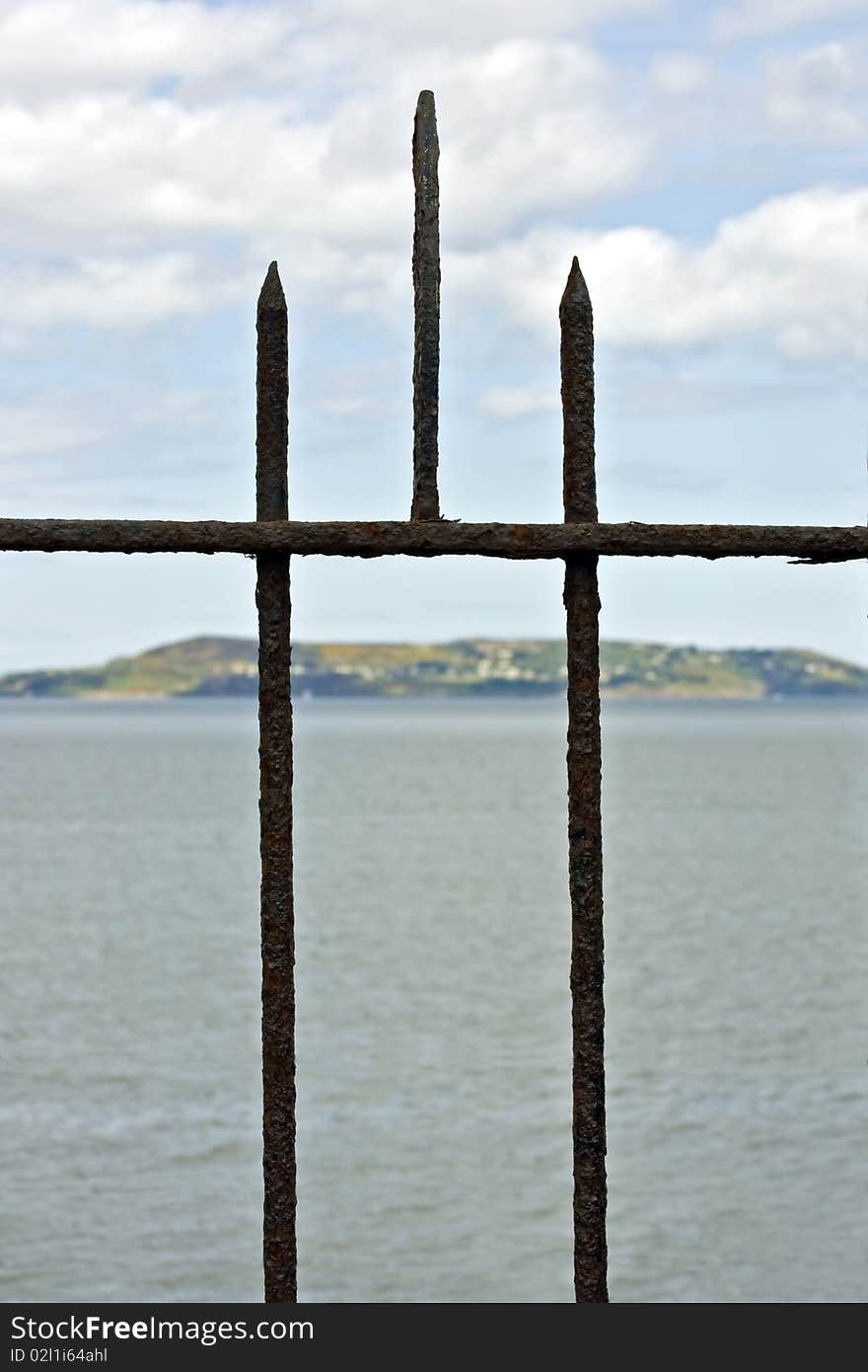 A detail of a rusty old fence in front of an island  seascape . A detail of a rusty old fence in front of an island  seascape