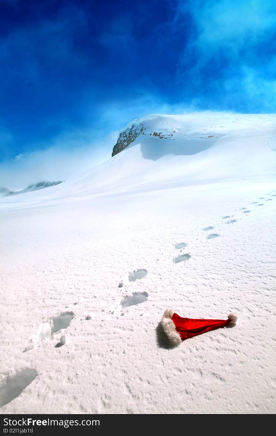 Santa's hat lying on a snow on a backgrounds of a mountains and blue sky. Santa's hat lying on a snow on a backgrounds of a mountains and blue sky