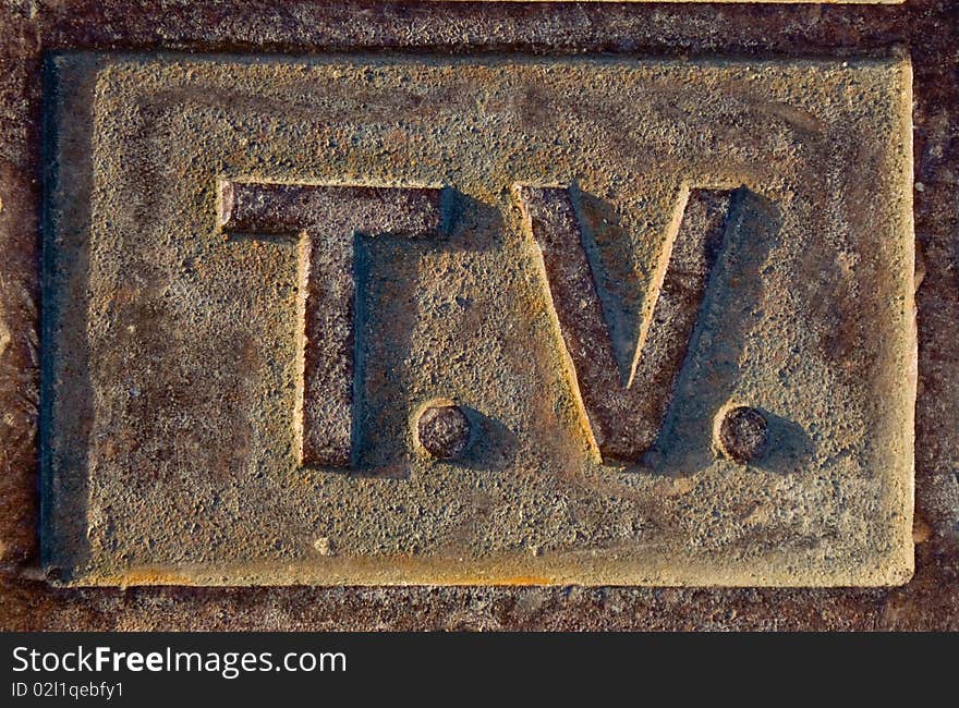 A metallic sign which is rusty and brown spelling TV. A metallic sign which is rusty and brown spelling TV