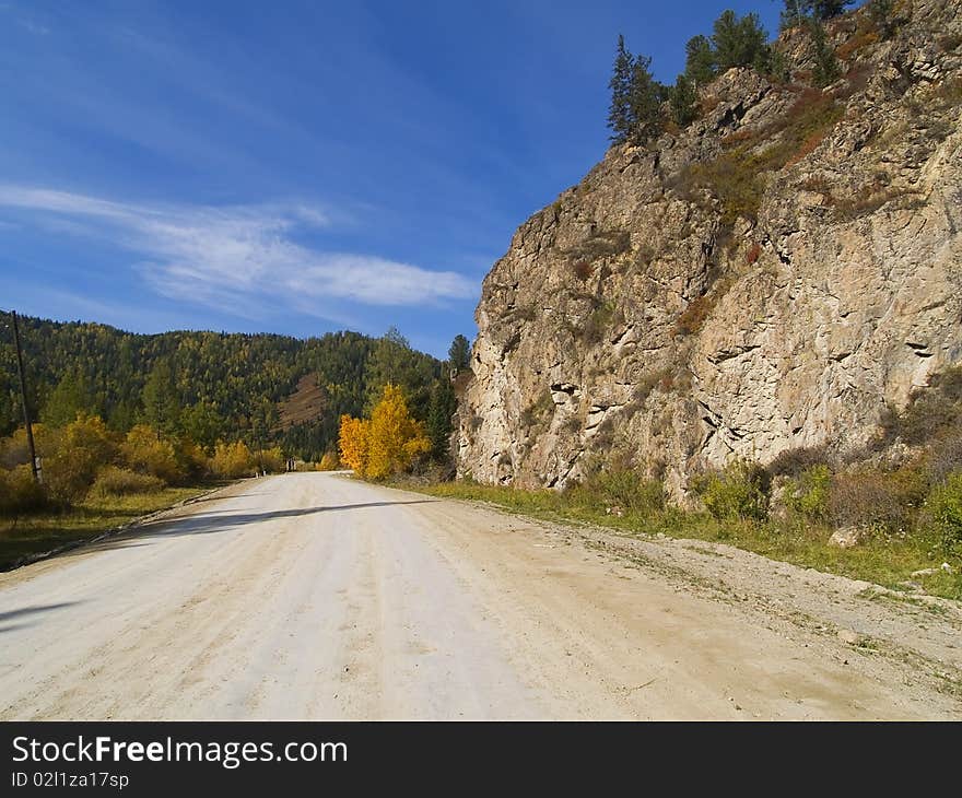 Dirt road in the mountains with forests, rocks and sky with clouds