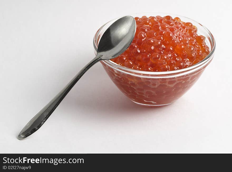 Red caviar in the little glass bow and spoon isolated over grey gradient background