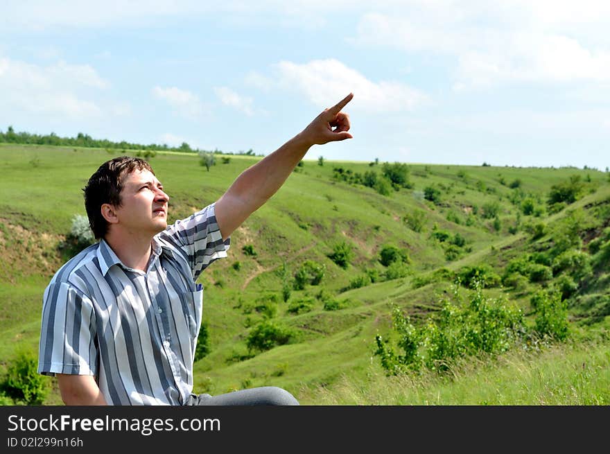 A young man sits and pointed his finger at the sky