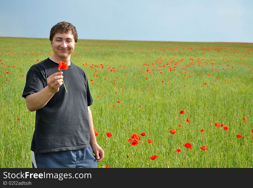 A young man holds a poppy flower, against a background of poppy field