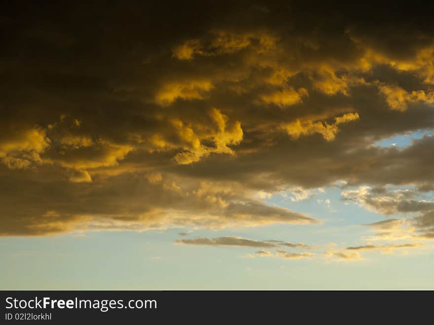 Dramatic storm clouds, colored partly orange due to the setting sun, with blue skies behind