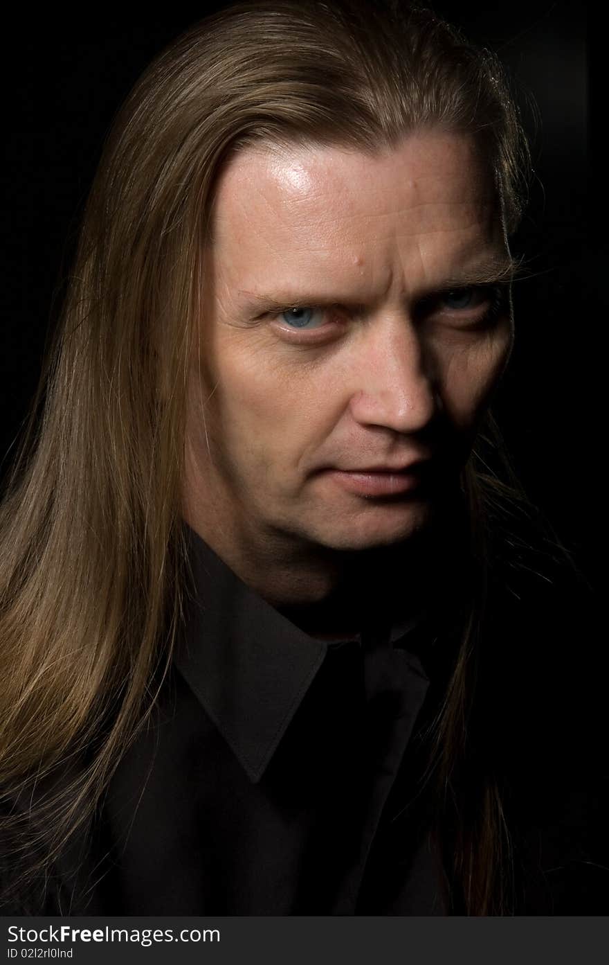 Portrait of serious man with long hair over a black background. Portrait of serious man with long hair over a black background