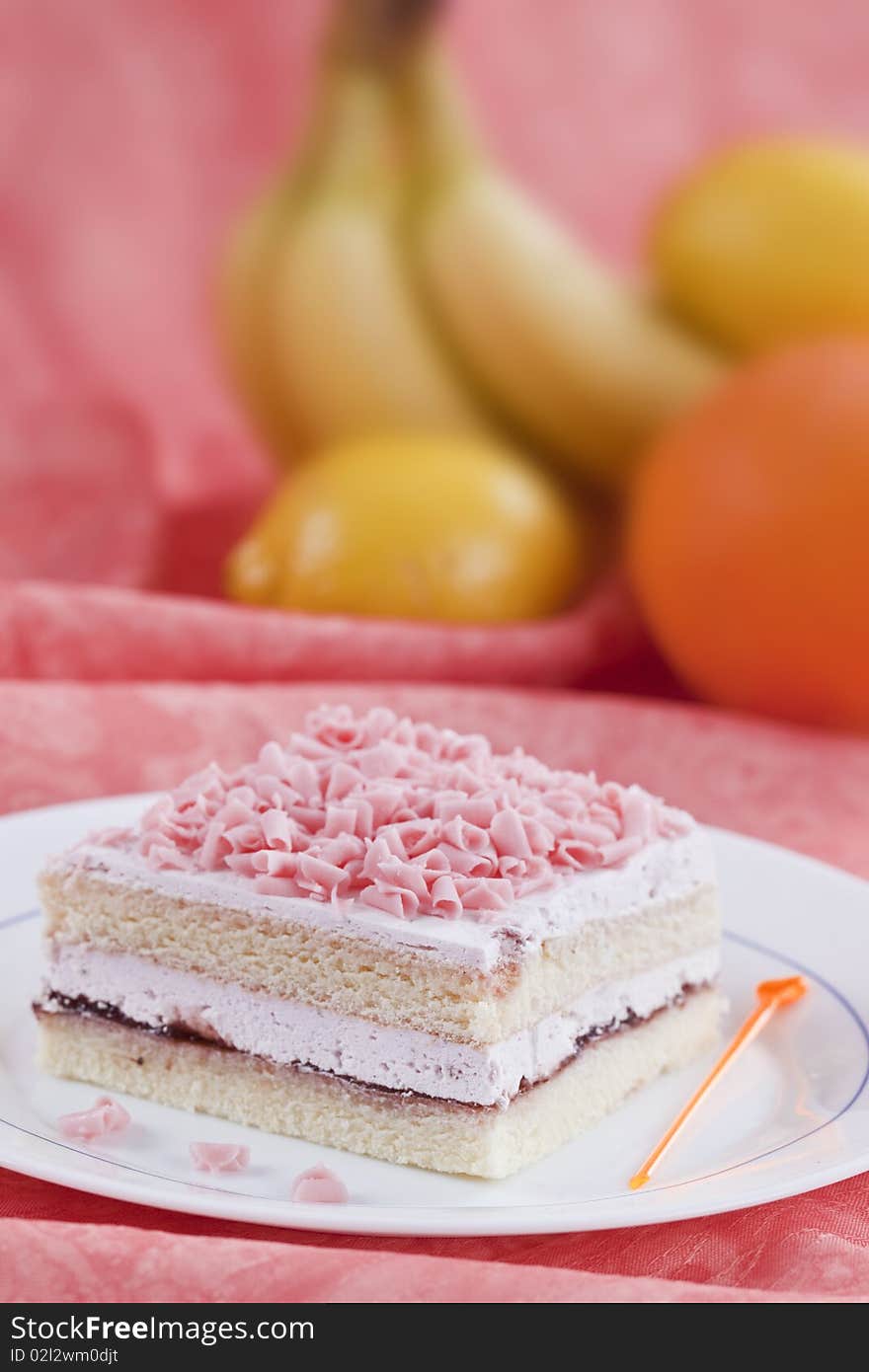 Slice of cake on white plate with some fruits on the background