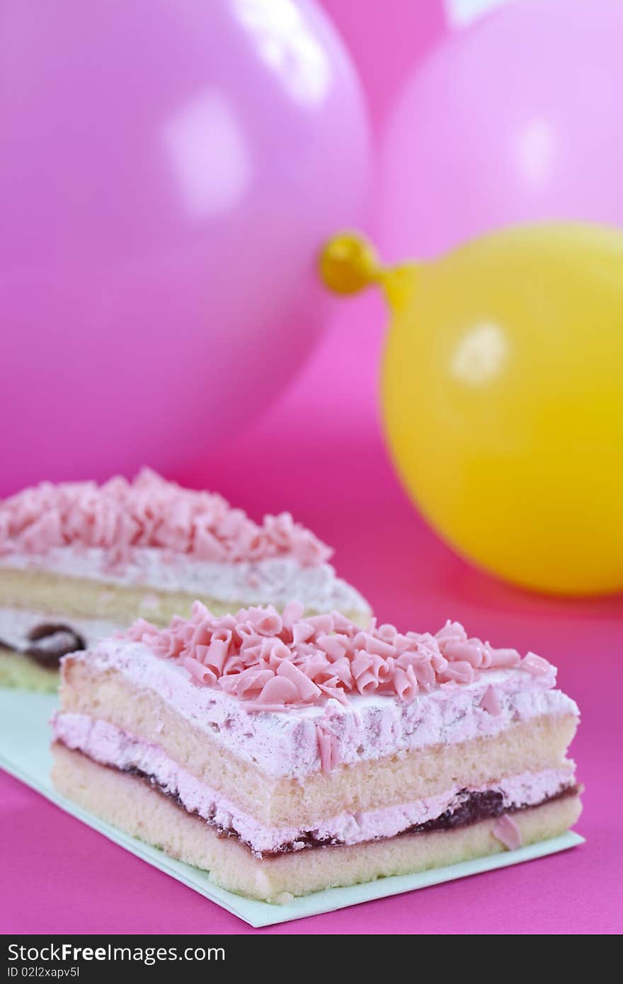 Close up of fresh cake on pink table top with some balloons on the background