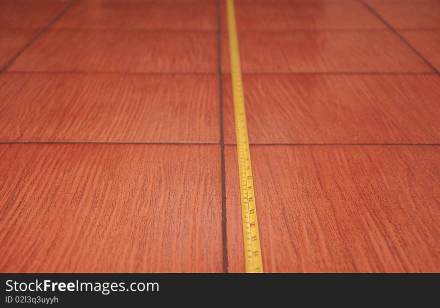 Square tile for floor of brown colour with ruler lying on it. Square tile for floor of brown colour with ruler lying on it