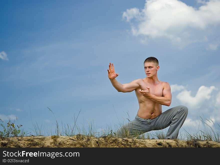 Young man in a karate pose in desert on cloudly sky background. Young man in a karate pose in desert on cloudly sky background