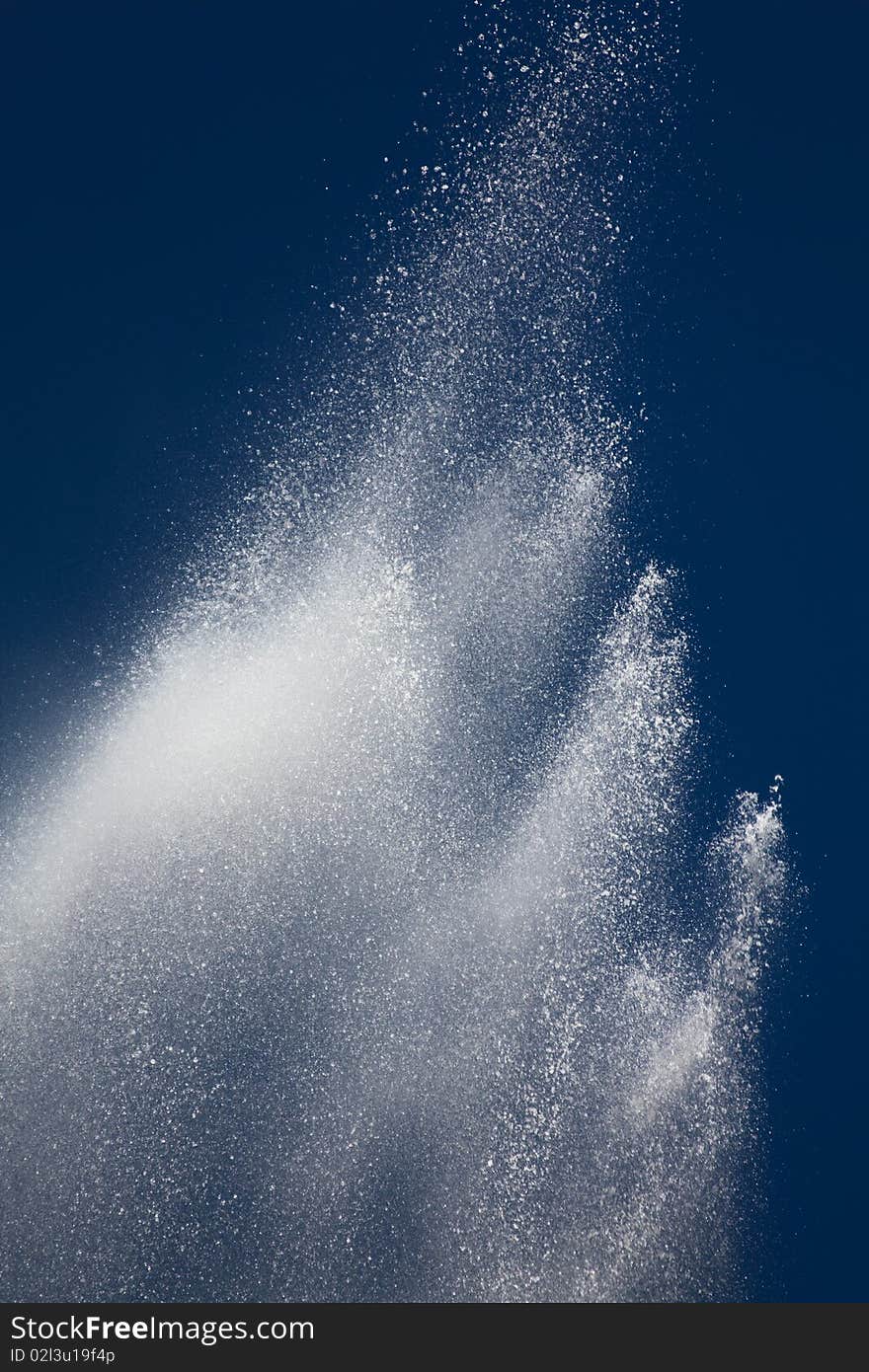 White splashes and drops of water from a fountain against the dark blue sky