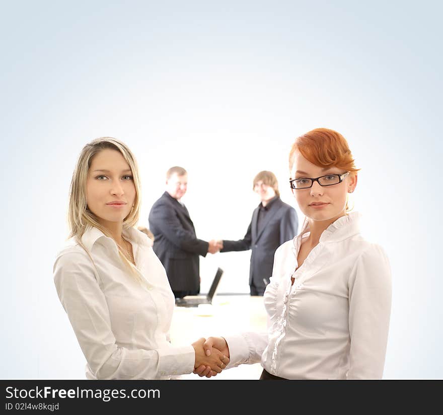 Two young business women are shaking hands in front of two business men. Image isolated on a light blue gradient background. Two young business women are shaking hands in front of two business men. Image isolated on a light blue gradient background.