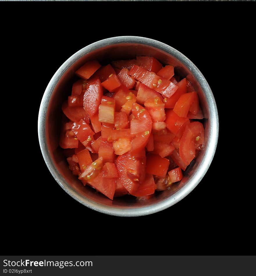 A bunch of sliced, diced, and cut red tomatoes inside of a round metal bowl isolated on pitch black background. A bunch of sliced, diced, and cut red tomatoes inside of a round metal bowl isolated on pitch black background.