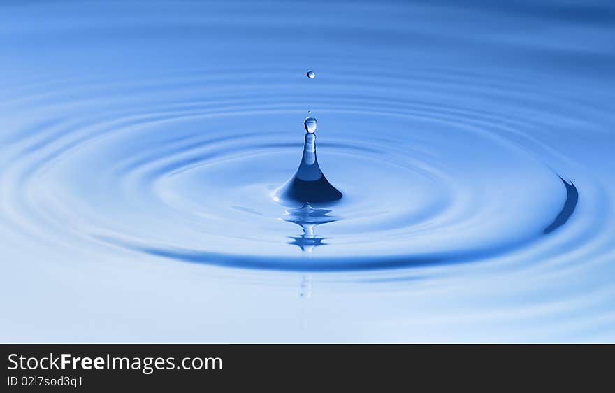 Clean blue drop of water splashing in clear water. Abstract blue background