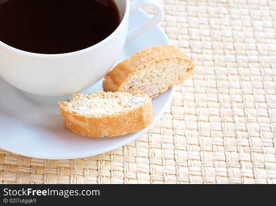 Cup of hot black coffee and baked almond biscotti cookies on woven straw placemat. Cup of hot black coffee and baked almond biscotti cookies on woven straw placemat