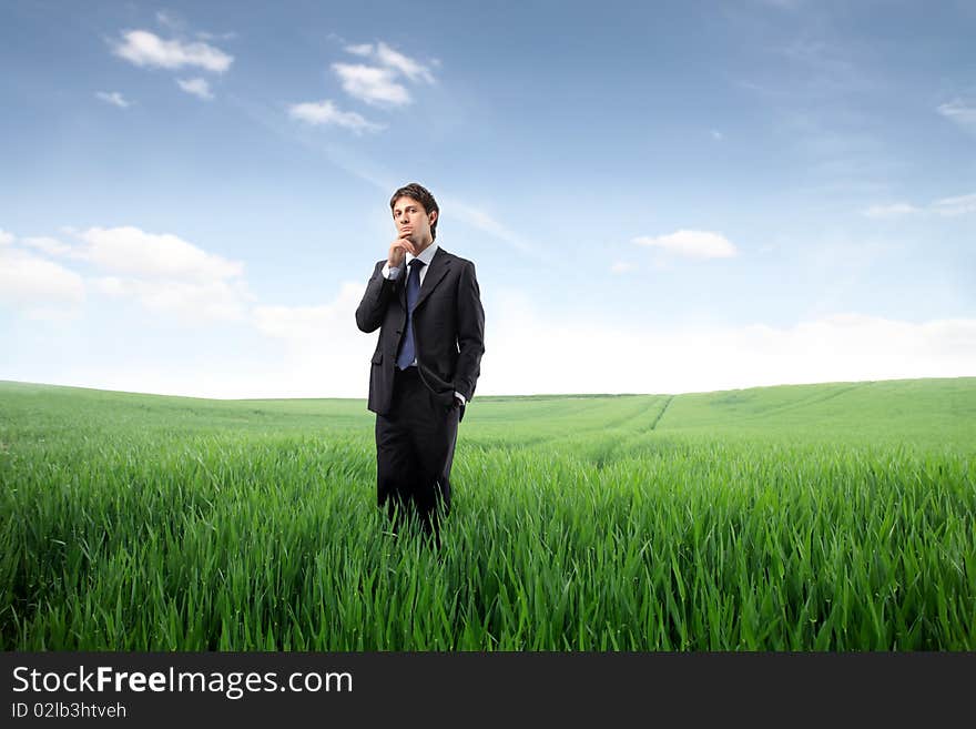 Businessman standing on a green meadow and reflecting. Businessman standing on a green meadow and reflecting