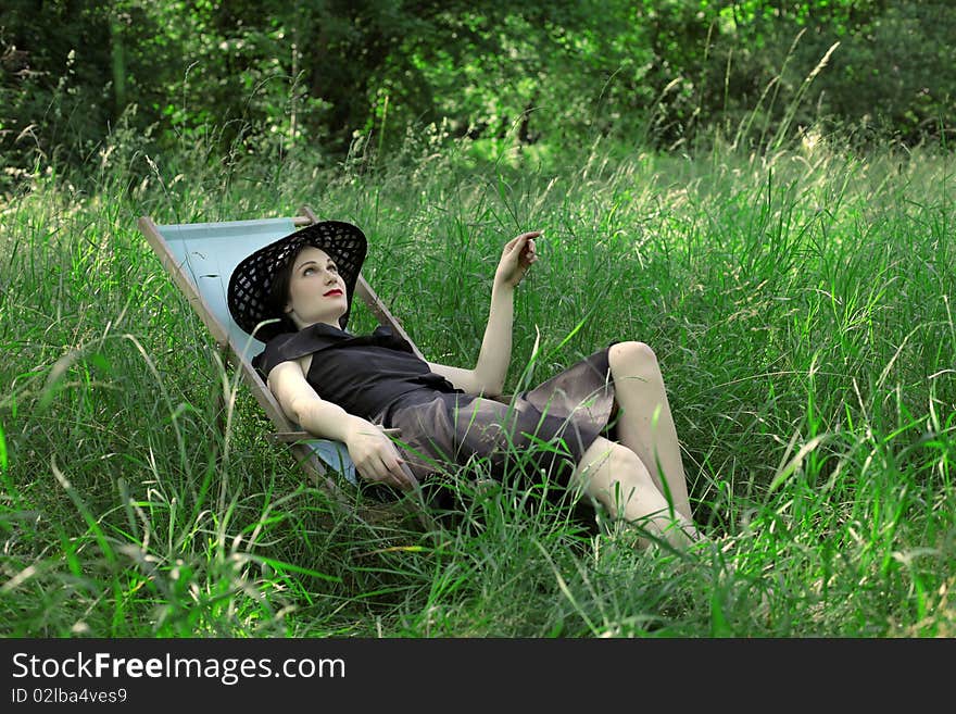 Young woman lying on a deckchair on a green meadow. Young woman lying on a deckchair on a green meadow