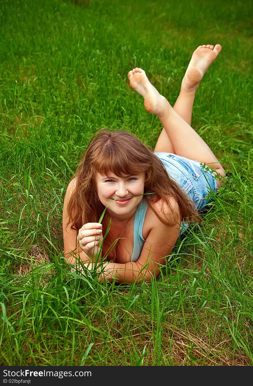 Portrait of a beautiful smiling female lying on a grass, it is summer and she is holding a blade of grass. Portrait of a beautiful smiling female lying on a grass, it is summer and she is holding a blade of grass