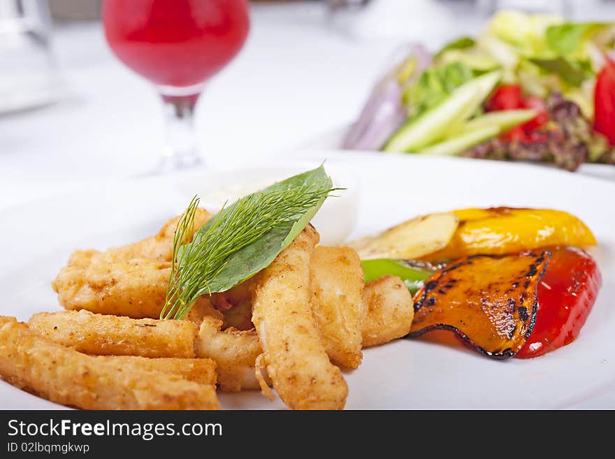 Fried calamari seafood meal with salad on a white plate with a fresh fruit drink