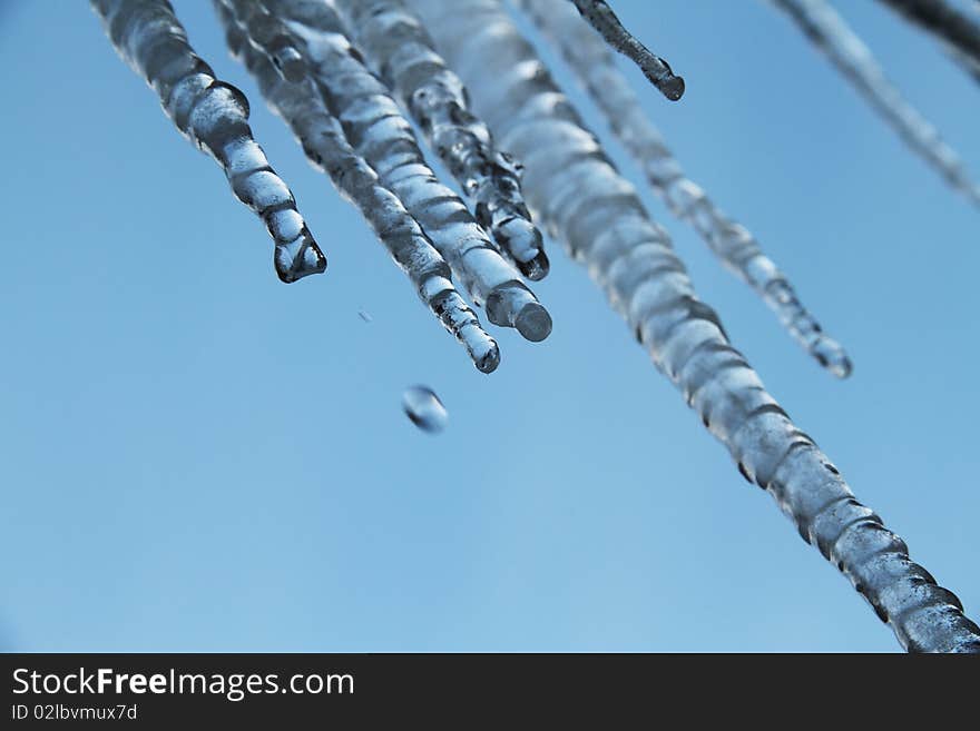 Icicles melting with dripping water in front of a blue sky. Icicles melting with dripping water in front of a blue sky.