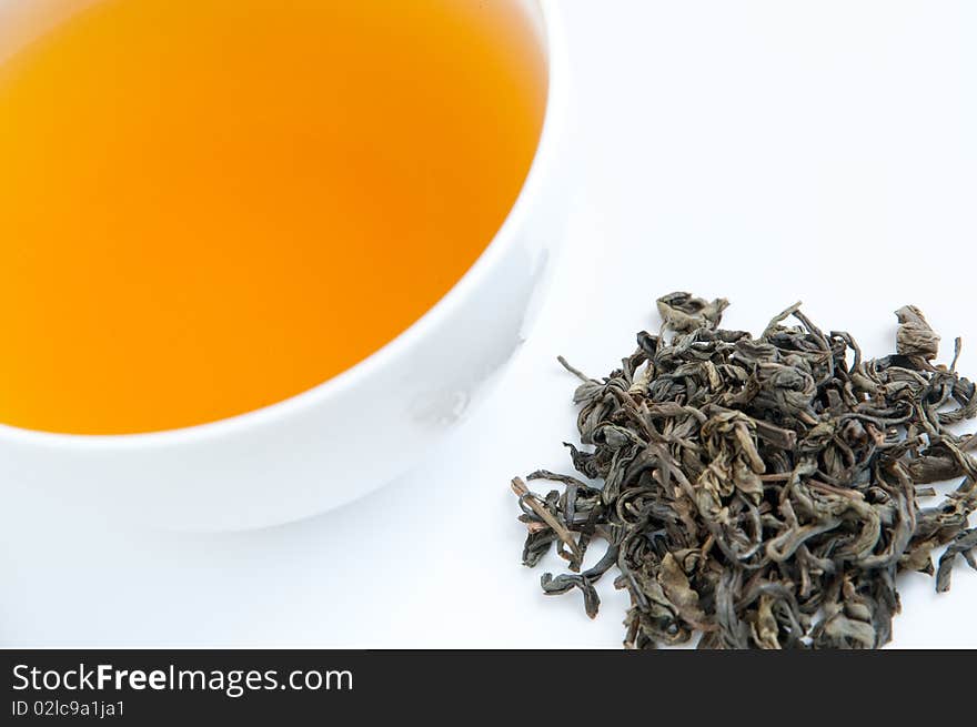 A cup of tea on a tray with dried tea leaves, isolated on white