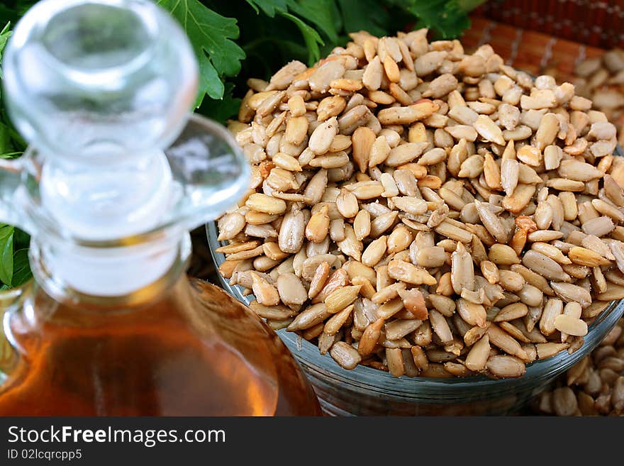 Oil from sunflower seeds in a glass bottle with the cleared sunflower seeds and a parsley branch.