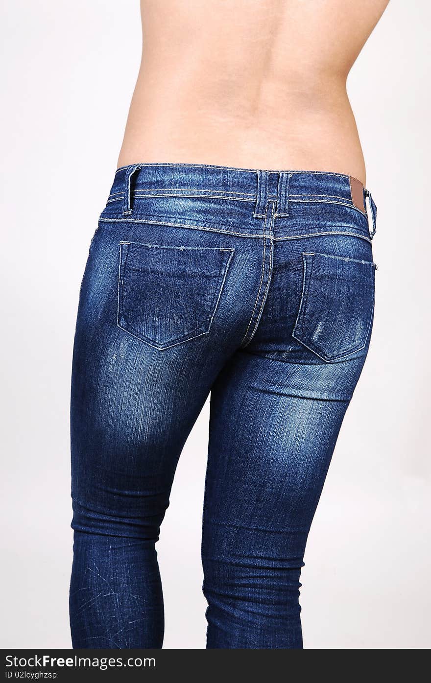 A topless Hispanic woman in jeans from the back, shooing her nice round butt, on light gray background. A topless Hispanic woman in jeans from the back, shooing her nice round butt, on light gray background.